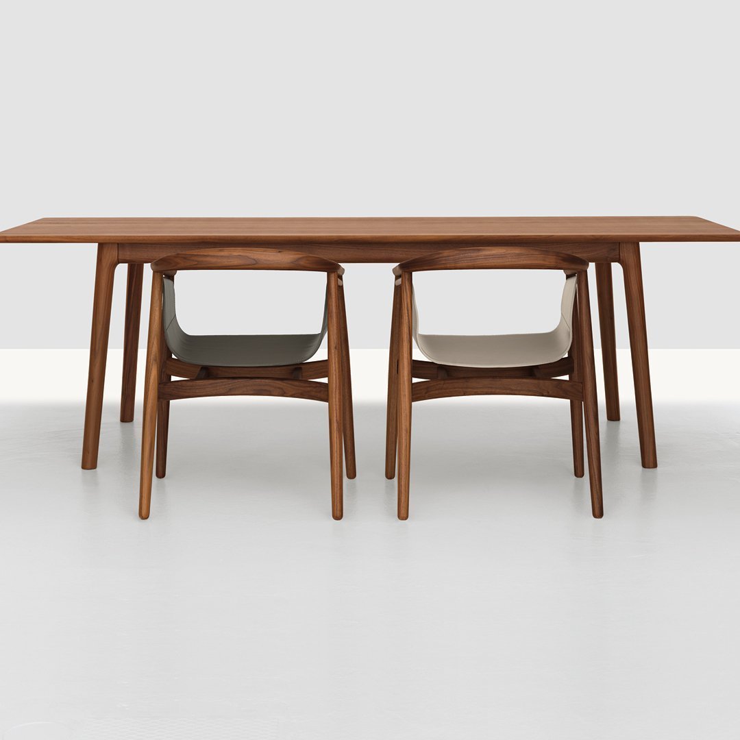 Wooden dining table with warm brown finish and two modern chairs in light gray and soft beige upholstery.