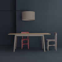 Modern dining set featuring a light wood table, pink and gray chairs, against a navy blue backdrop with a beige lamp.