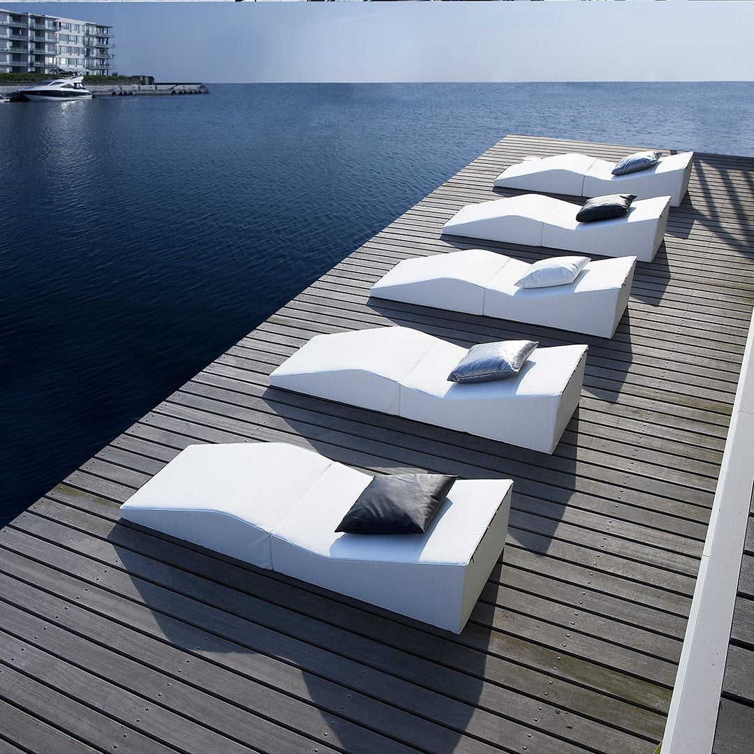 Stylish white lounge chairs with black cushions, featuring sleek, modern curves against a serene water backdrop.