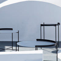 Modern design circular tables with black metal frames and light gray tabletops against a white backdrop.