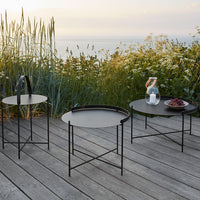 Black metal side tables with sleek designs, featuring circular tops and minimalist patterns against a natural outdoor backdrop.