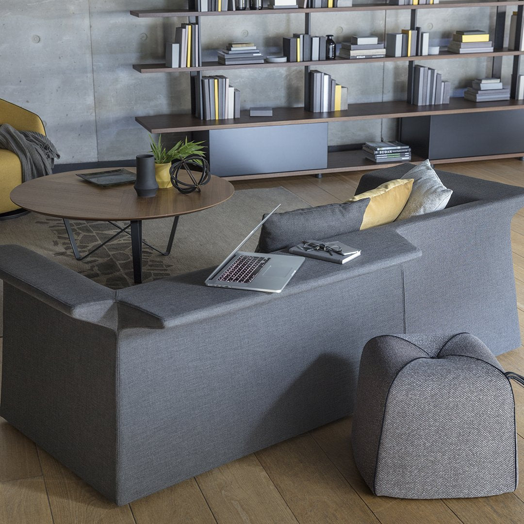 Modern gray sofa with angular design, accented by yellow cushions and a textured bean bag against a warm wood floor.