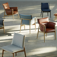Assorted chairs in brown, blue, and light gray, featuring a mix of leather and fabric textures against a minimalist background.