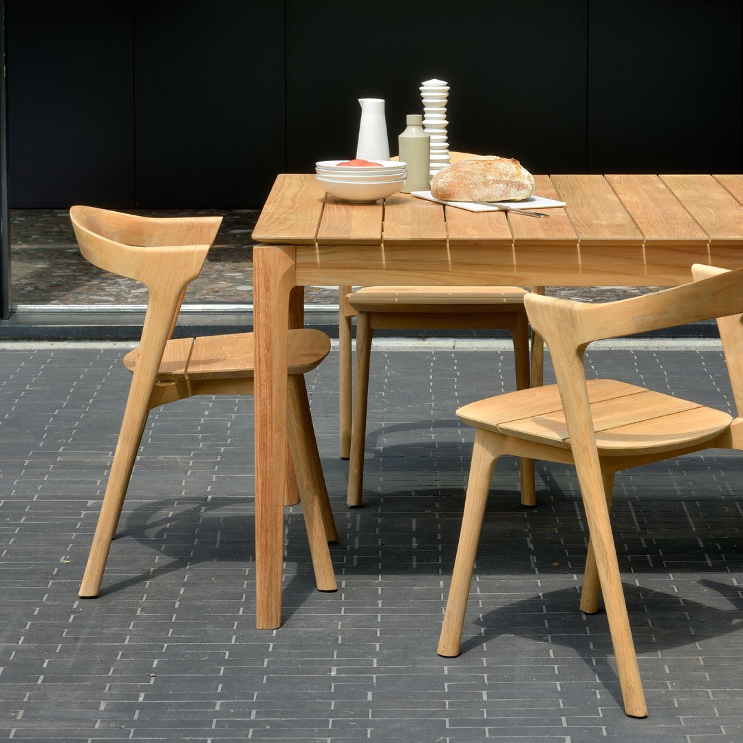Natural wood dining table and chairs with light beige tones, showcasing a sleek, modern design on a textured black surface.