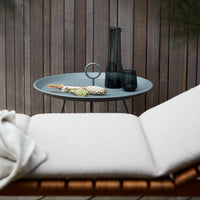 Stylish gray serving tray with black glassware on a wooden table next to a beige lounge chair and white throw.