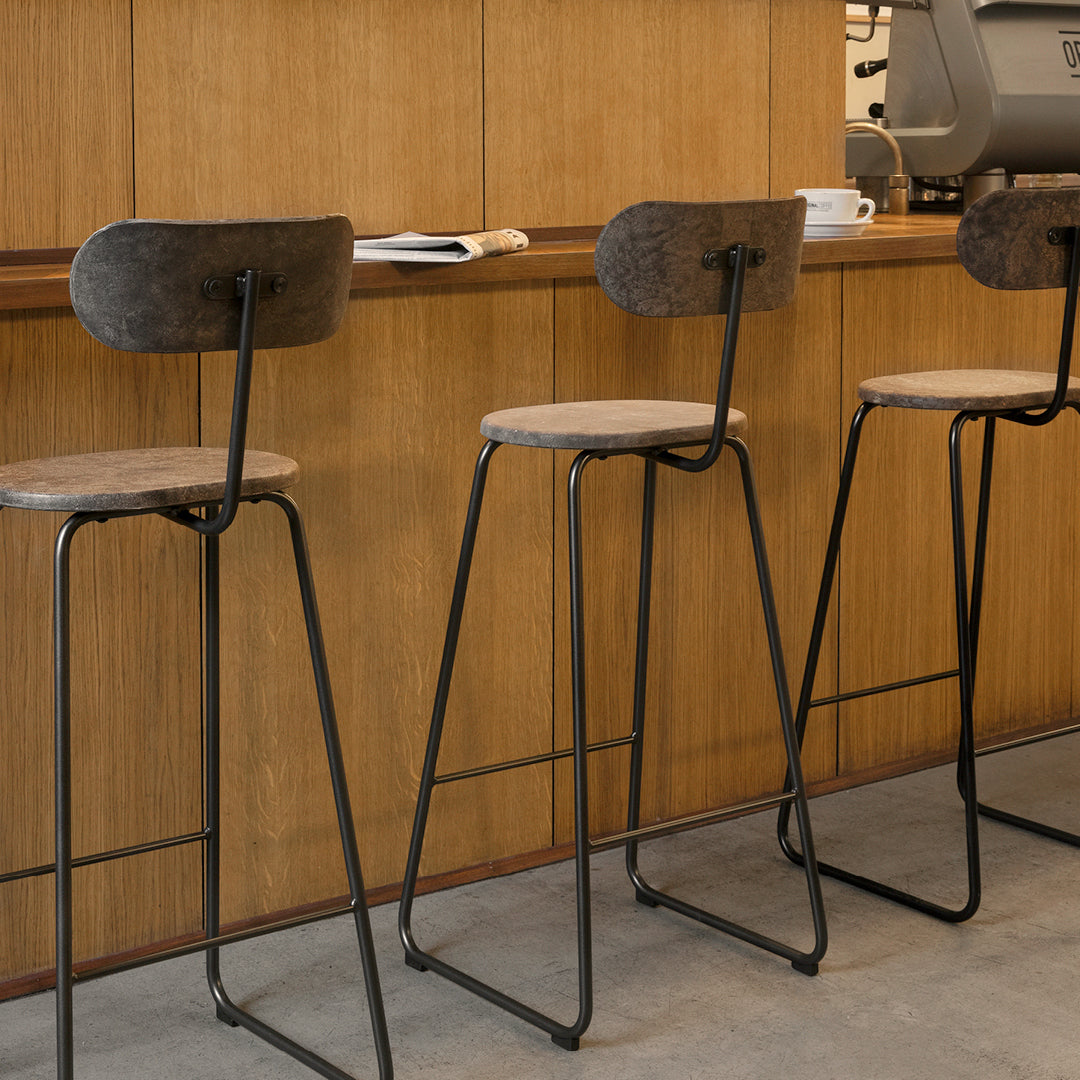 Set of three modern bar stools with black metal frames and grey padded seats against a wooden backdrop.