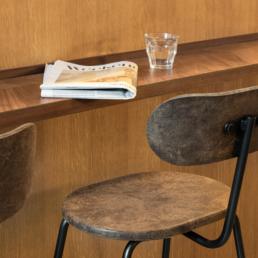 Brown textured chair with a smooth black metal base, minimalist design against a warm wooden backdrop.
