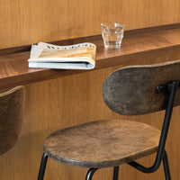 Brown textured chair with a smooth black metal base, minimalist design against a warm wooden backdrop.