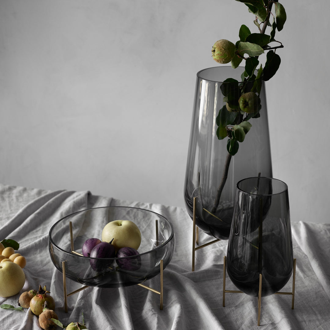 "Set of glass vases in smoky gray with gold stands, displayed on a textured silver tablecloth."