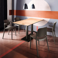 Modern wooden dining table with a light finish, surrounded by sleek gray chairs on a patterned red and beige floor.