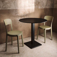 Round black table with minimalist design paired with olive green chairs against a warm, textured background.