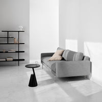 Gray sofa with striped cushions, modern black side table, and minimalist decor in a light, airy space.