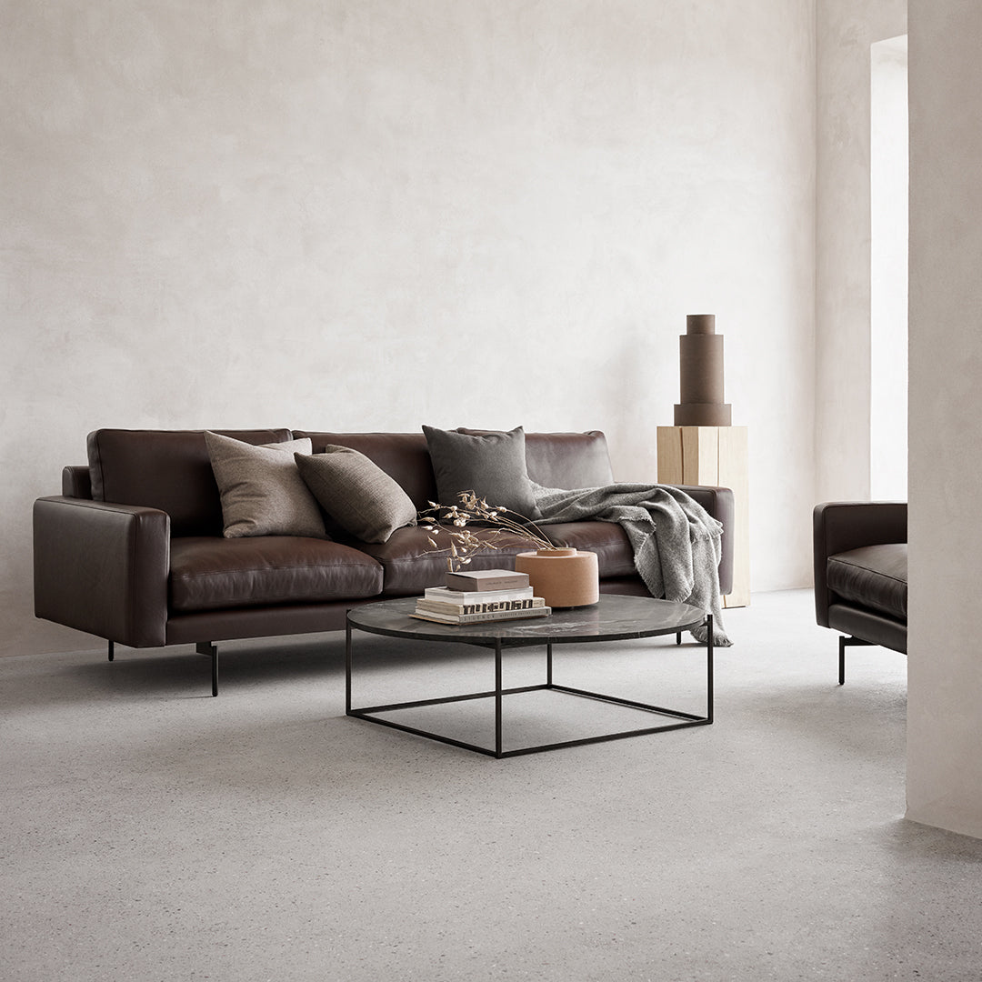 Dark brown leather sofa with gray cushions, complemented by a minimalist black coffee table in a neutral room.
