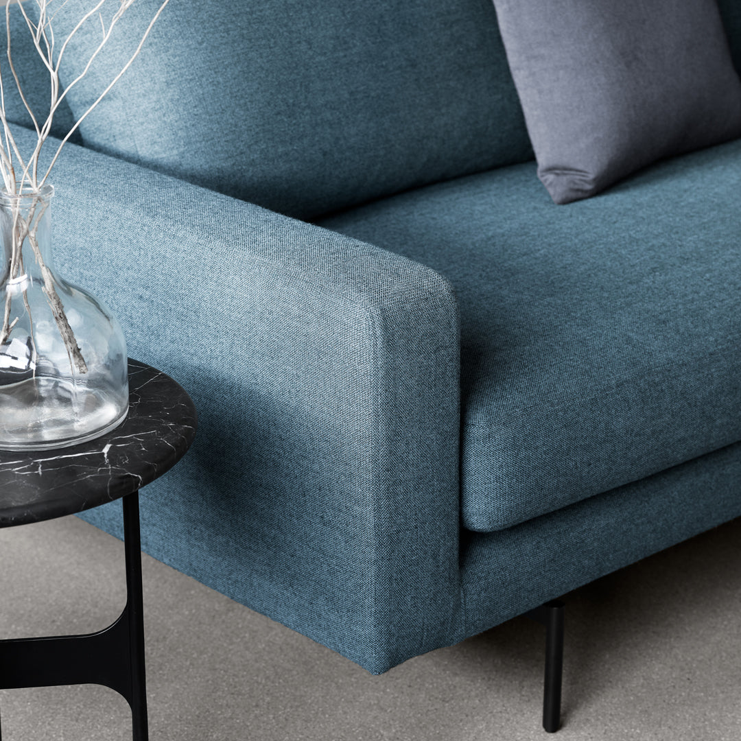 Textured blue sofa with a sleek design, paired with a round black table. Soft gray patterns enhance modern decor.
