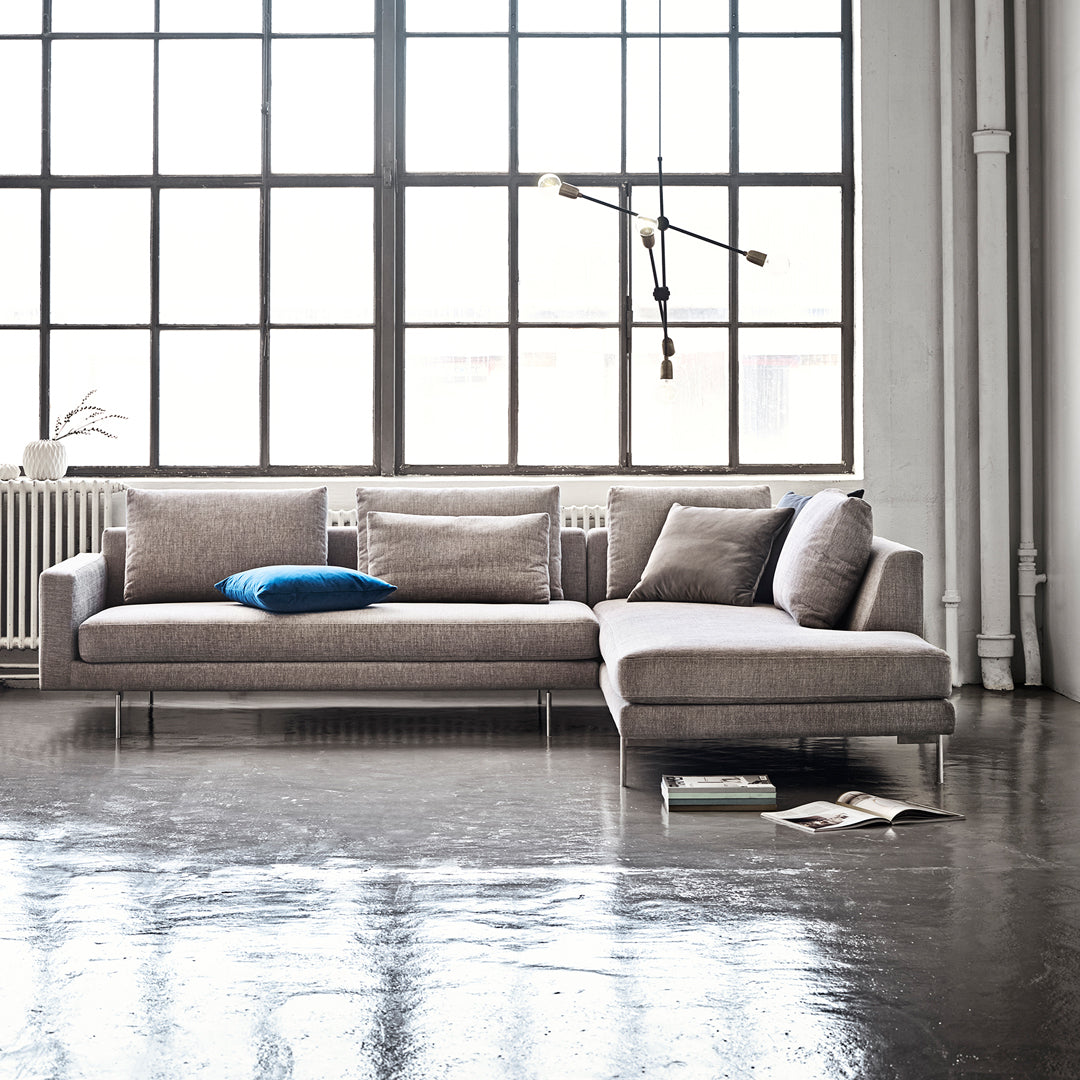 Light gray sectional sofa with subtle texture, accented by a vibrant blue throw pillow against a minimalist backdrop.