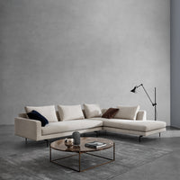 Beige sectional sofa with blue and brown accent pillows, paired with a round metal coffee table on a gray concrete floor.