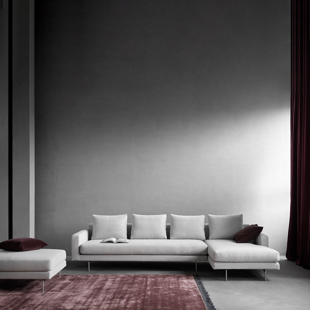 Modern gray sectional sofa with plush cushions, accented by a deep burgundy rug and rich maroon curtains.