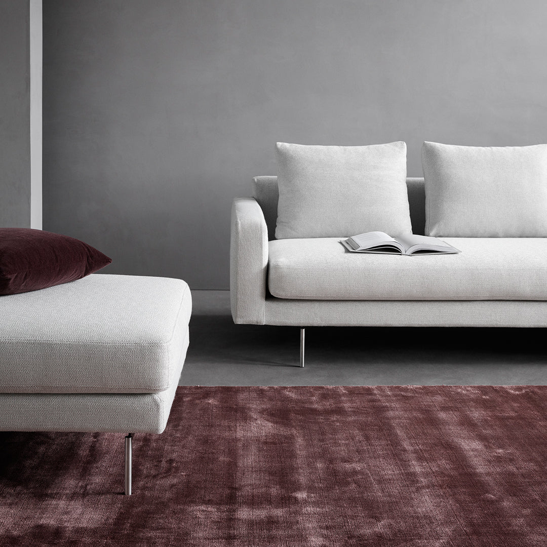 Minimalist gray sofa set with light gray upholstery, accented by a deep burgundy rug and contrasting white pillows.