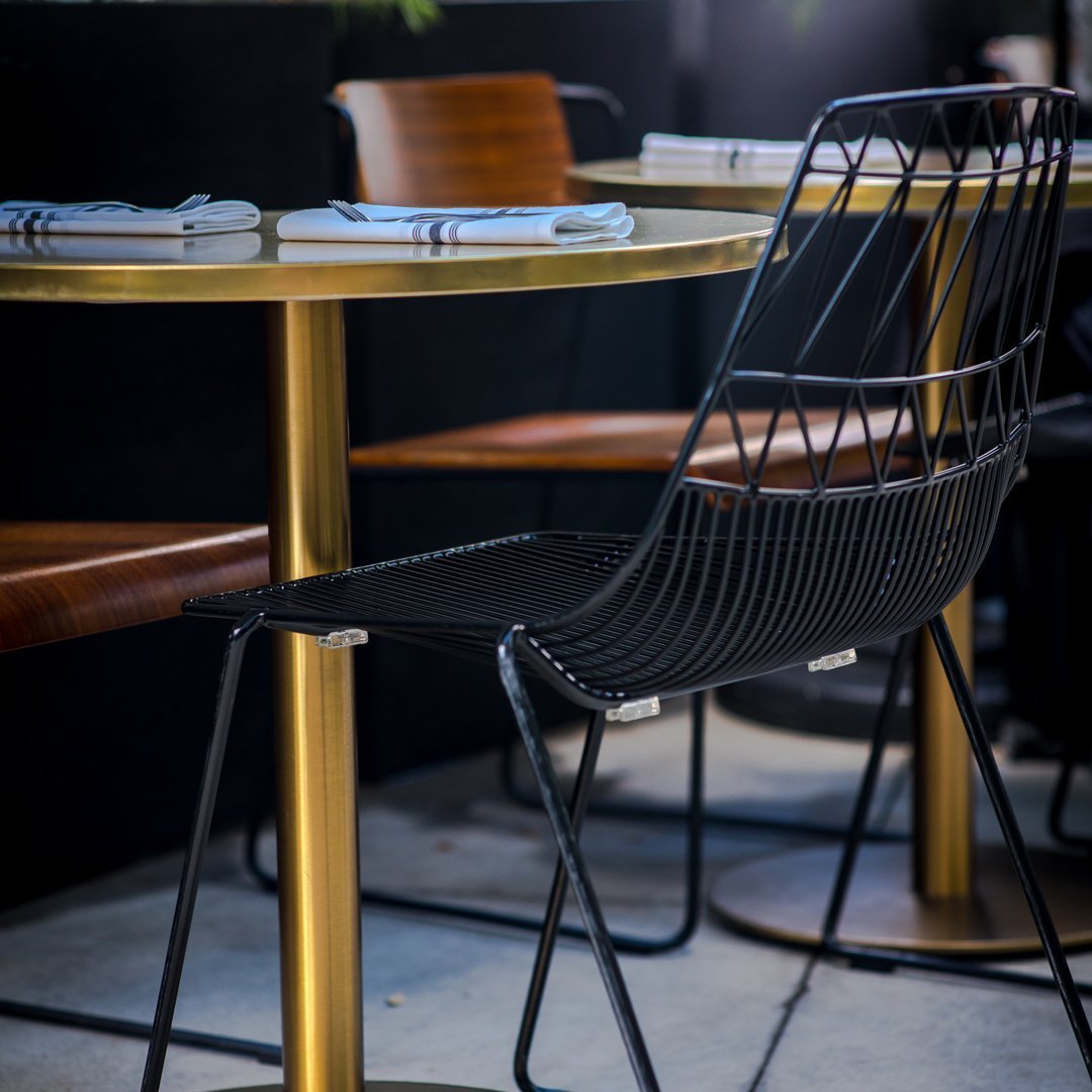 Stylish black wire chair and gold round table, enhanced by wooden accents in a modern dining setup.