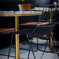 Stylish black wire chair and gold round table, enhanced by wooden accents in a modern dining setup.