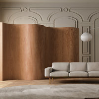 Light beige sofa with smooth texture, warm wood panel backdrop, and soft gray patterned rug on a light wood floor.