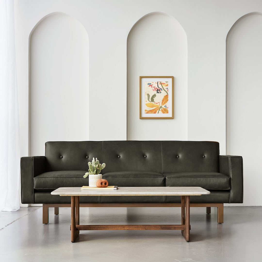 Dark green leather sofa with subtle button tufting against a neutral wall, complemented by warm wood accents.