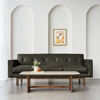 Dark green leather sofa with subtle button tufting against a neutral wall, complemented by warm wood accents.