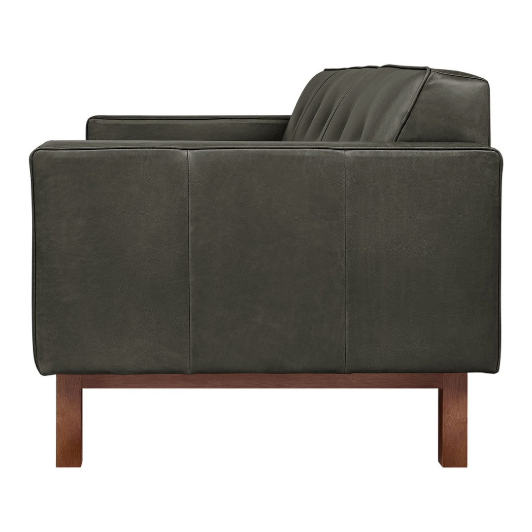 Dark green leather sofa with a matte finish and sleek wood legs, featuring subtle horizontal tufting.