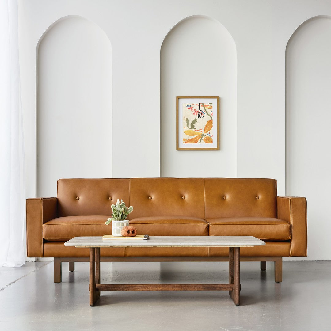Brown leather sofa with button details, paired with a white marble and wood coffee table in a neutral-toned room.