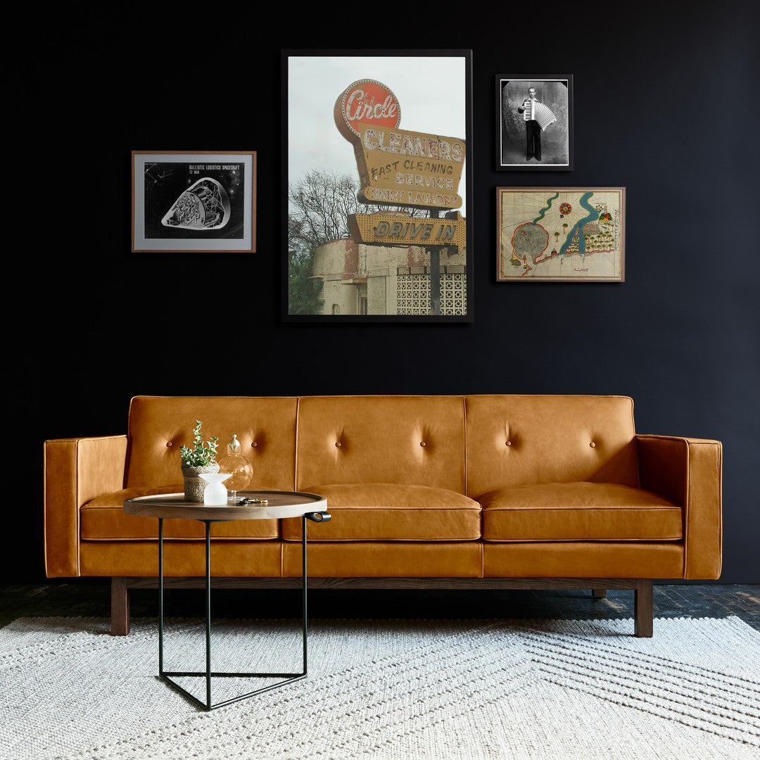 "Mid-century modern orange leather sofa with button tufting, set against a black wall and neutral rug."
