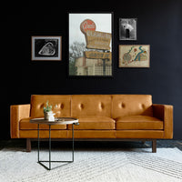 "Mid-century modern orange leather sofa with button tufting, set against a black wall and neutral rug."
