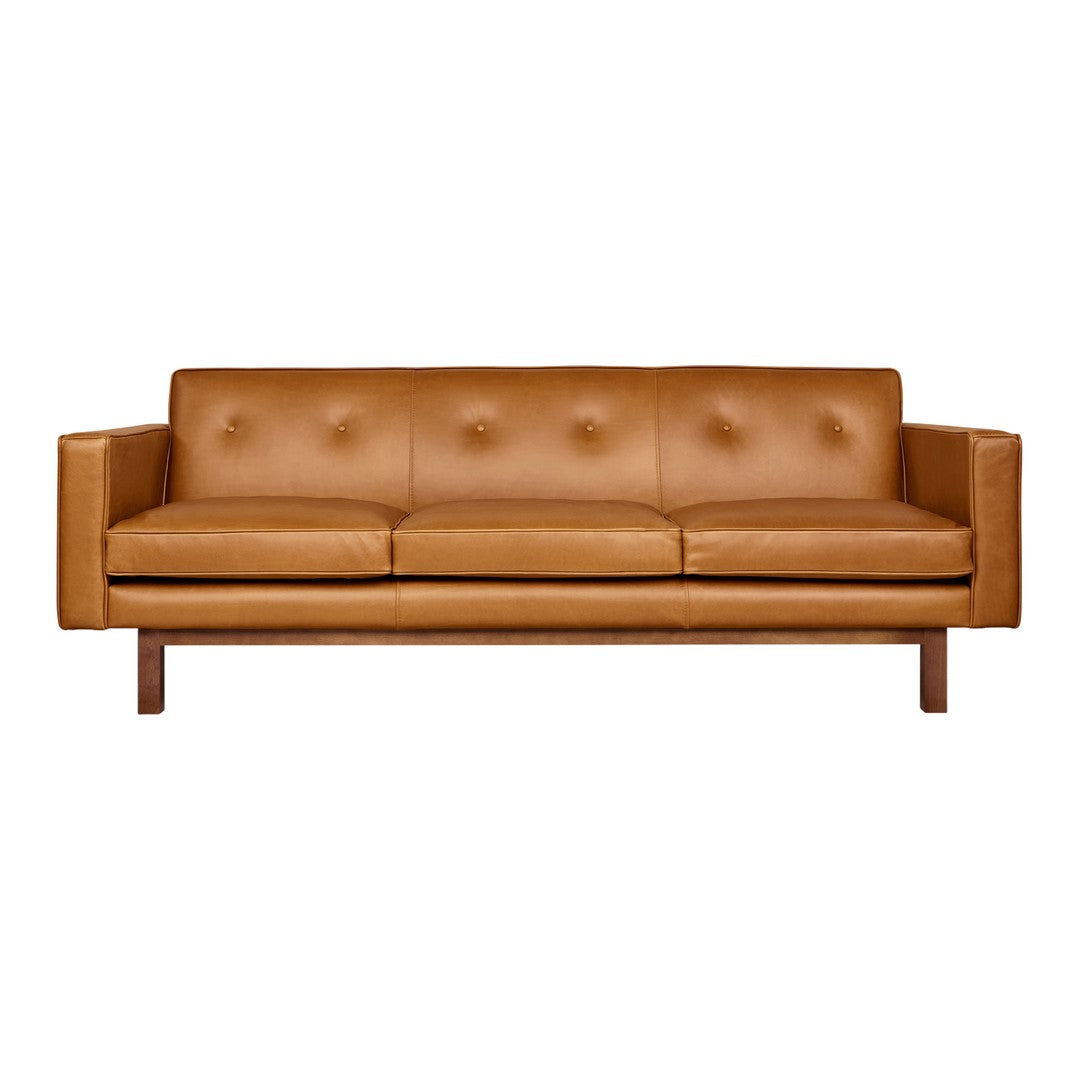 Brown leather sofa with button tufting and wooden legs, showcasing a sleek, modern design.
