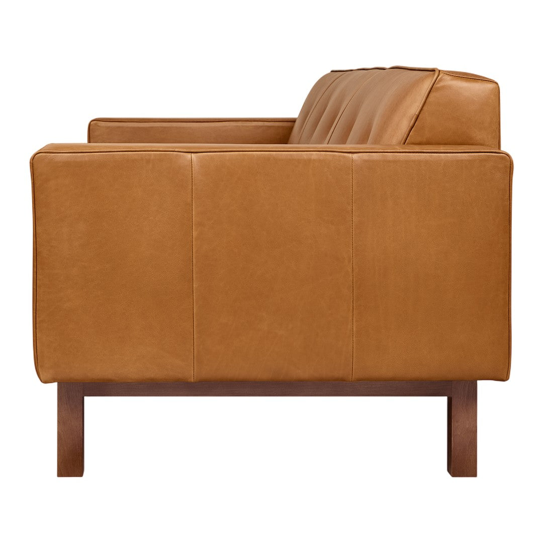 Tan leather sofa with a smooth texture and subtle quilted design, paired with dark wooden legs.