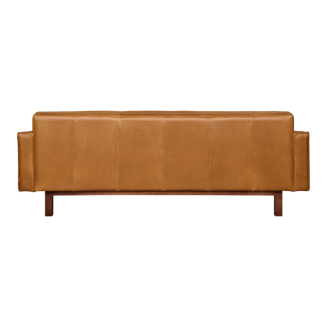Brown leather sofa with a smooth, matte finish and vertical panel stitching on a wooden base.