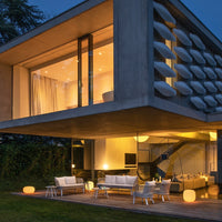 "Modern outdoor furniture set in white with soft lighting against a sleek concrete backdrop, illuminated by warm hues."