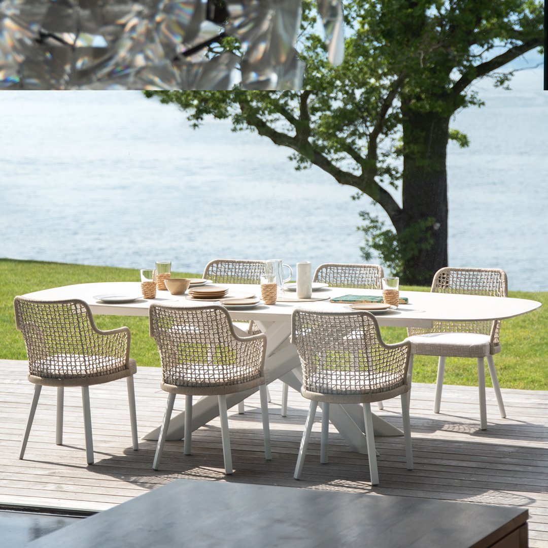 Stylish outdoor dining set featuring woven light beige chairs and a smooth white table against a serene blue water backdrop.