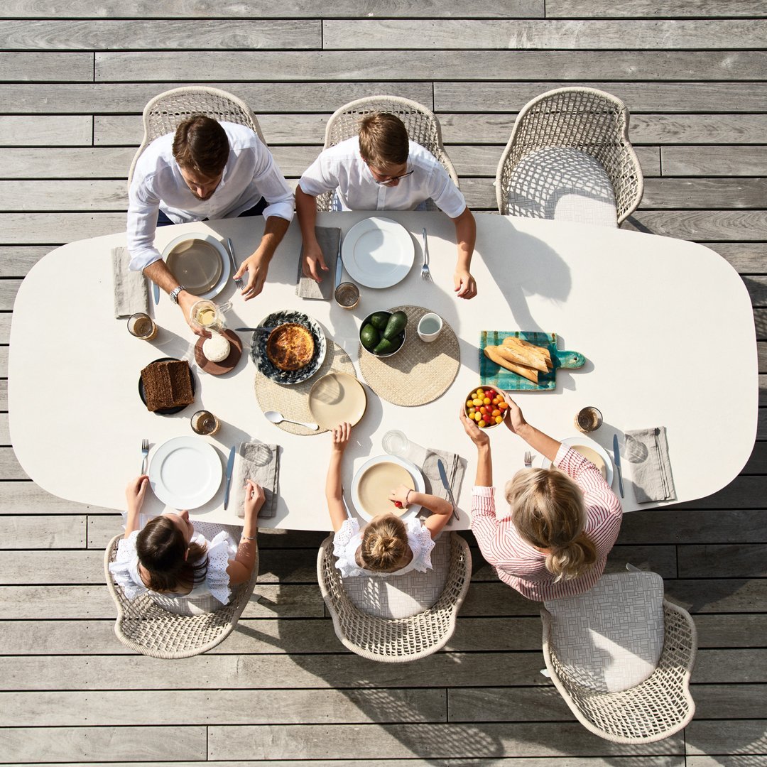 "Elegant white table setting with neutral and pastel colors, featuring woven chair patterns and a wooden deck."