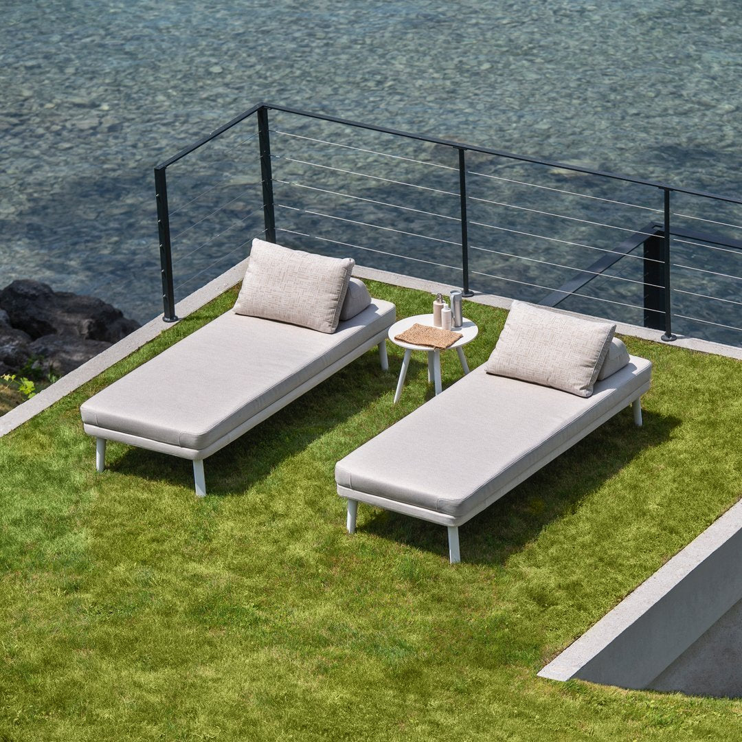 "Light gray pool loungers with textured cushions on green grass, paired with a small white side table."