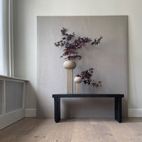 Minimalist beige backdrop with purple foliage in round ceramic vases on a black wooden table, enhancing color contrast.