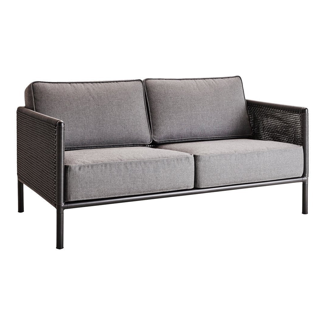 Gray upholstered two-seater sofa with black metal frame and woven side detail. Modern and stylish design.