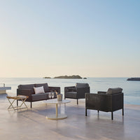 Modern outdoor seating featuring dark gray cushions and a minimalist beige table, set against a tranquil seascape.
