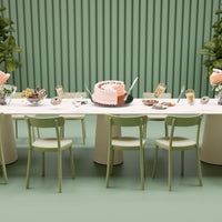 Elegant pastel pink and green dining setup with a white table, featuring stylish chairs and decorative elements.