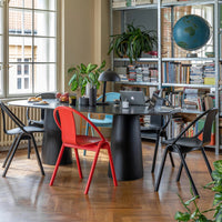 Black round table with red and blue chairs, surrounded by green plants and bookshelves, creating a vibrant, modern atmosphere.