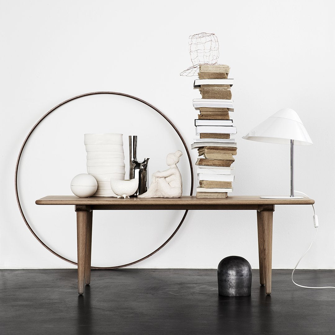 Natural wood table with a minimalistic design, featuring neutral tones, white, and soft textures against a black floor.