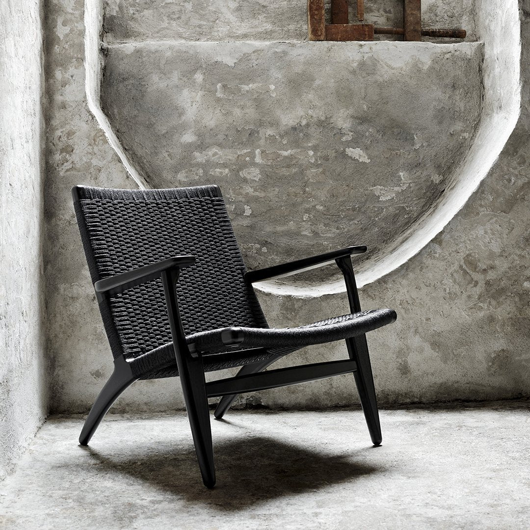Black woven chair with a sleek design, set against a textured gray concrete background.