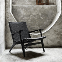 Black woven chair with a sleek design, set against a textured gray concrete background.
