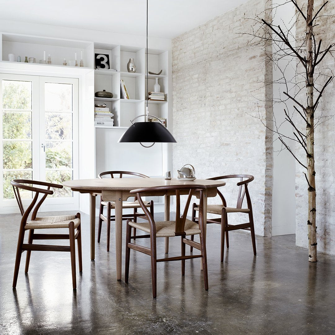 Wooden dining table with brown chairs, minimalist design, and a black pendant light against a light textured wall.