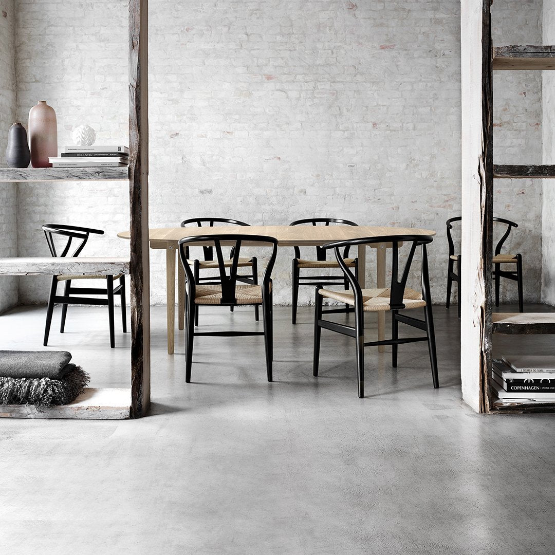 "Minimalist dining room featuring black wooden chairs and a natural wood table against a textured gray backdrop."