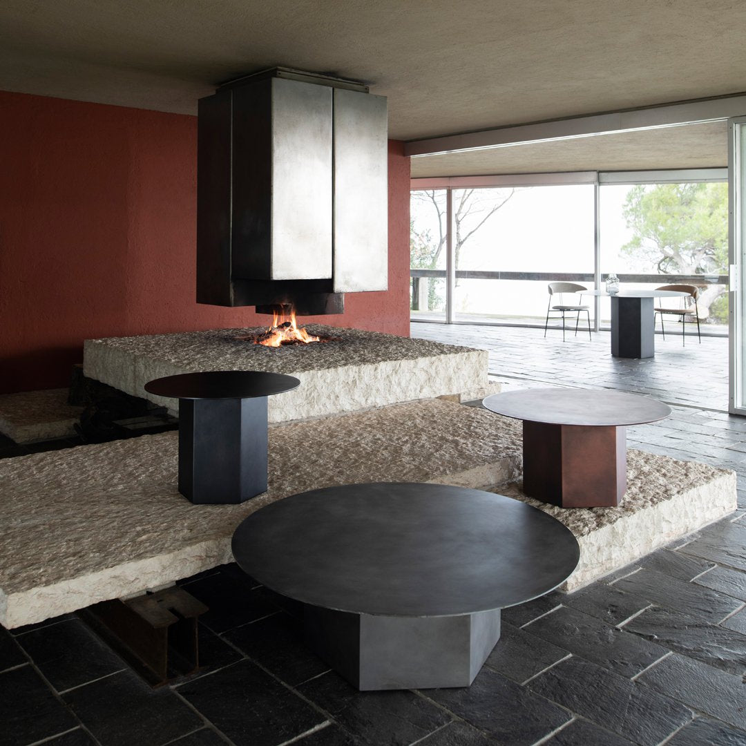 Stylish round coffee tables in matte black and rust with minimalist design, set against textured stone and warm red walls.