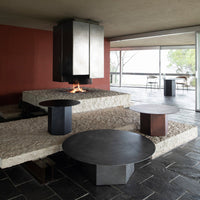 Stylish round coffee tables in matte black and rust with minimalist design, set against textured stone and warm red walls.